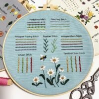 The Embroidery Stitch Practice Kit 6 features a light blue fabric in a hoop showcasing labelled stitches—Palestina, couching, whipped running and back, feather, chain, and twisted chain—with daisies and a bee embroidered at the bottom.