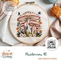 The Mushroom 10: Hand embroidery pattern features two large mushrooms with leaves and flowers on white fabric. Includes thread painting, stumpwork instructions, and is designed by Daydream Stitchery.