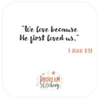 Text in script font reads: We love because He first loved us. Below, 1 John 4:19 is written in orange. At the bottom, Daydream Stitchery’s floral logo appears, featuring the ‘He first loved us’: Hand embroidery patterns.